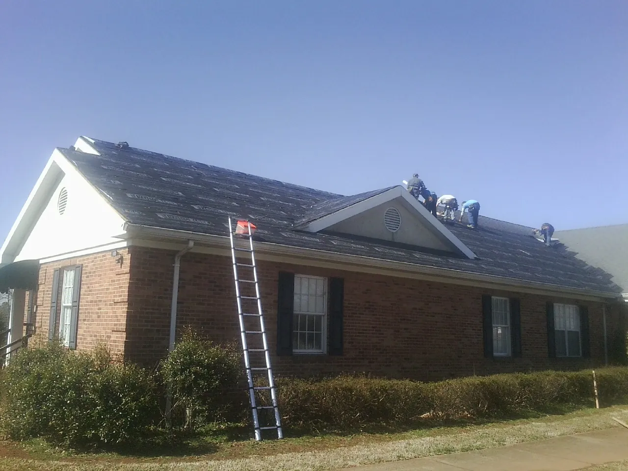 Crew tearing shingles off a brick ranch roof with a ladder set — Emergency Roof Repair work by our crew in Coward