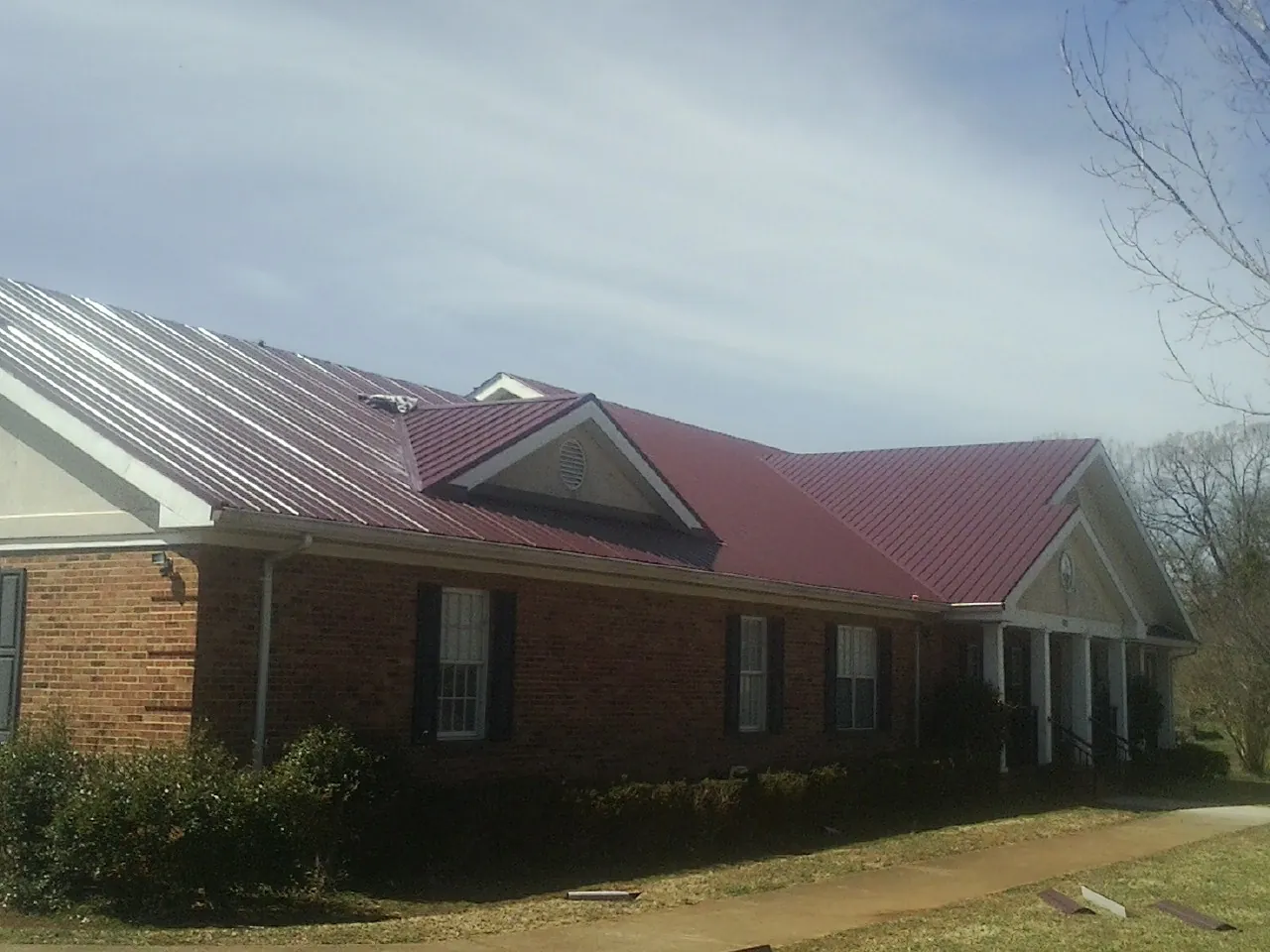 Red metal roof with gabled entries on a long brick building, from a Hail Damage Roof Repair job in Coward