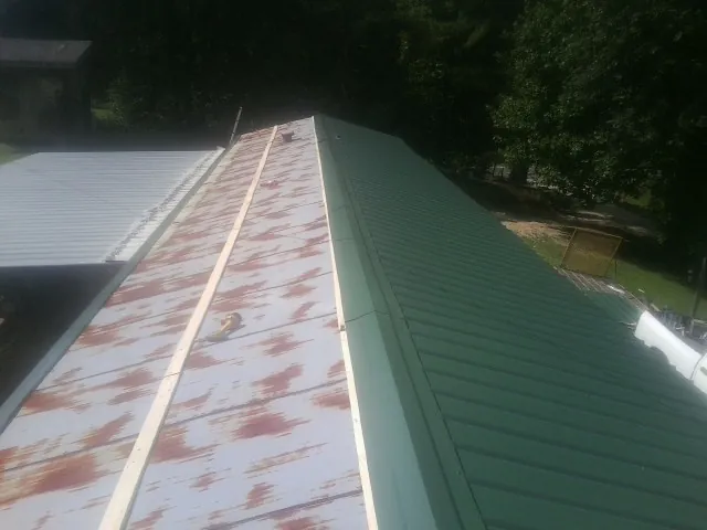 Old rusted panels beside newly installed green metal roofing — Wind Damage Roof Repair by Roofing Brothers in Coward