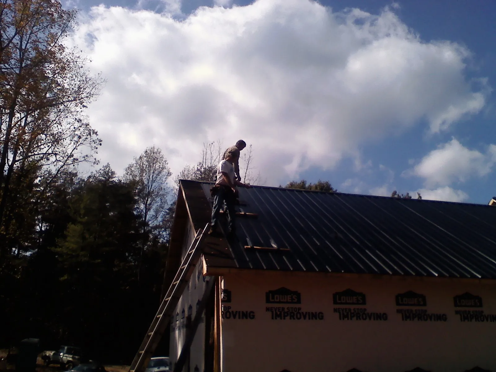 Roofer fastening dark metal panels high against a cloudy sky, from a Roof Inspection job in Coward