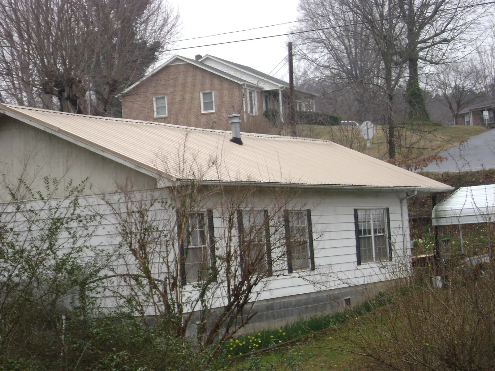 Tan metal roof on a white sided house set into a hillside — Commercial Roofing by Roofing Brothers in Coward