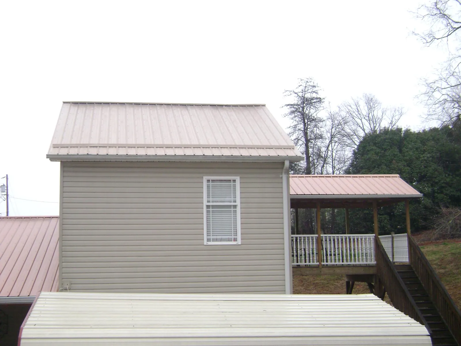 Tan metal roofs on a two story addition and attached porch, from a Roof Replacement job in Coward